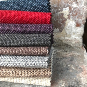 May include: A stack of eight fabric swatches in various colours and textures, including navy blue, red, purple, grey, brown, beige, and white. The swatches are arranged in a vertical stack, with the navy blue swatch on top and the white swatch on the bottom.