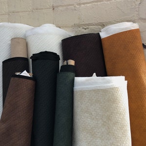 May include: A collection of fabric rolls in various colors and textures, including brown, black, white, and orange. The fabric has a woven pattern.
