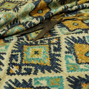 Op de afbeelding: Close-up van een beige stof met een geometrisch patroon in blauw, geel en groen. Een gouden schaar ligt op de stof.