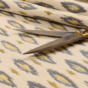 May include: Close-up of a pair of silver scissors lying on a cream-coloured fabric with a repeating pattern of yellow and grey ovals.