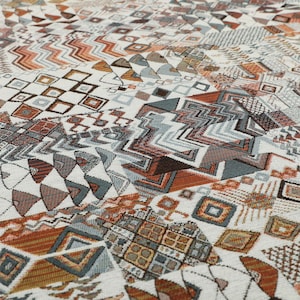 Peut inclure: Gros plan sur un tissu blanc avec un motif géométrique coloré. Le motif présente diverses formes, notamment des carrés, des triangles et des zigzags. Les couleurs sont principalement le brun, l'orange et le bleu.