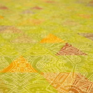 May include: Close-up of a lime green fabric with a repeating pattern of orange and brown triangles. The triangles are filled with intricate designs, and the background features a detailed, white, geometric pattern.