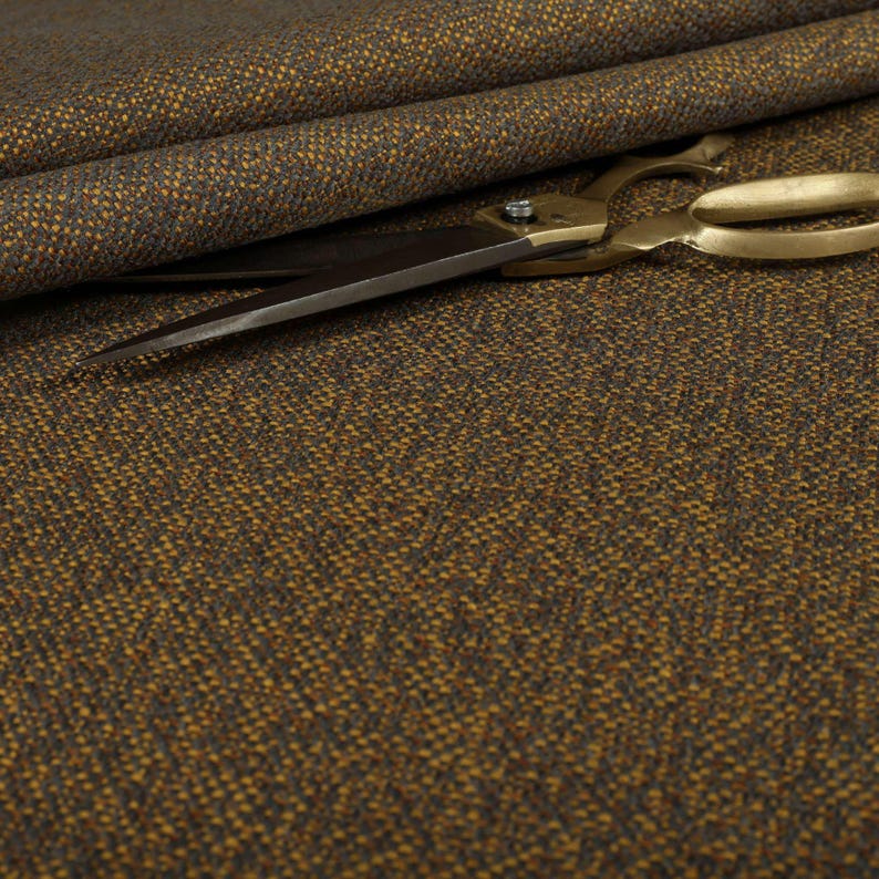 Puede incluir: Primer plano de tela de tweed marr&oacute;n y dorado con un tejido texturizado. Unas tijeras doradas descansan sobre la tela, con las hojas abiertas. La tela est&aacute; doblada en el fondo.