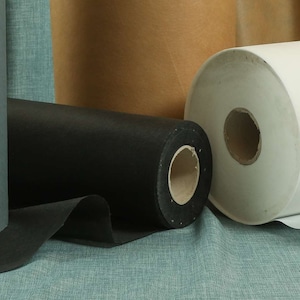 May include: Three rolls of fabric, one grey, one black, and one white. The rolls are on a blue textured surface.