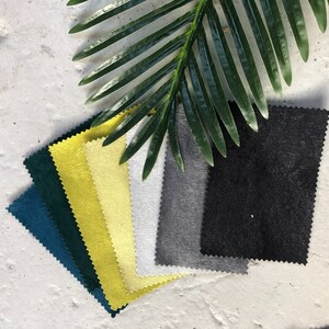 May include: A collection of fabric swatches in various colors, including teal, yellow, white, gray, and black. The swatches are arranged in a fan shape and are lying on a white surface.