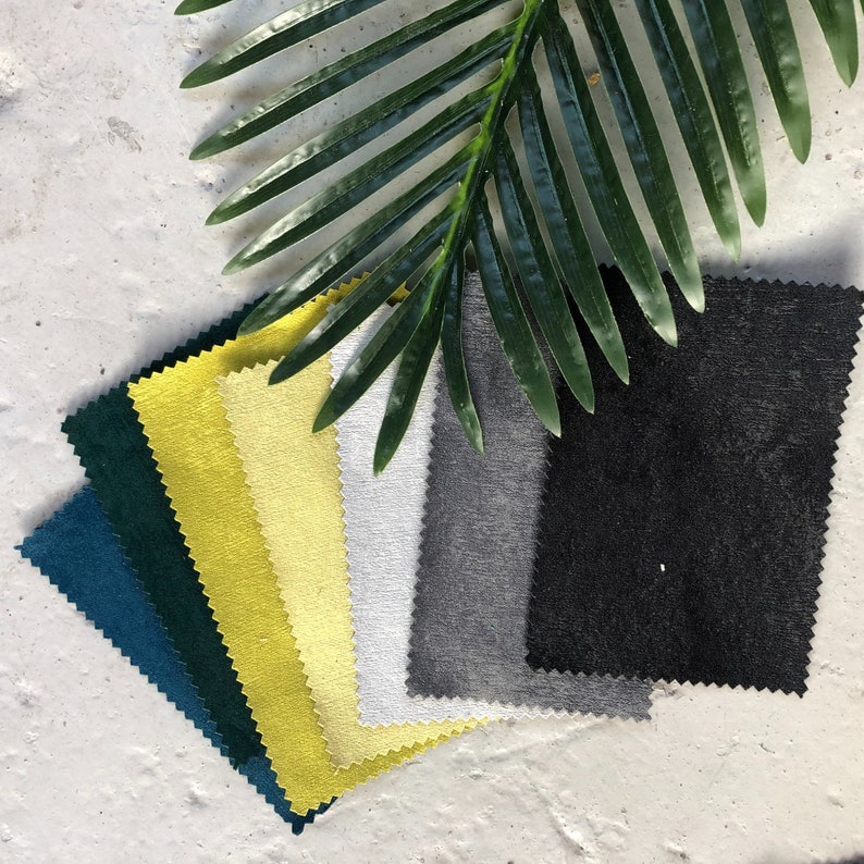 May include: A collection of fabric swatches in various colors, including teal, yellow, white, gray, and black. The swatches are arranged in a fan shape and are lying on a white surface.
