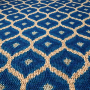 Könnte beinhalten: Nahaufnahme eines blau-beigen Stoffes mit Muster. Das Design zeigt ein sich wiederholendes geometrisches Muster aus Rauten in verschiedenen Blautönen, umrandet von beigen Linien. Der Stoff hat ein strukturiertes Aussehen.