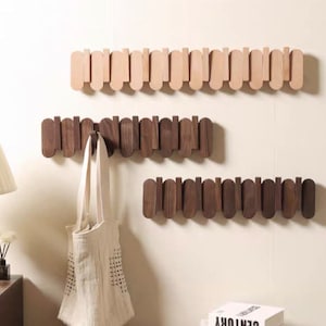 May include: Three wooden wall mounted coat racks with a staggered design. The top rack is light brown, the middle rack is dark brown, and the bottom rack is dark brown. A white tote bag hangs on the middle rack.