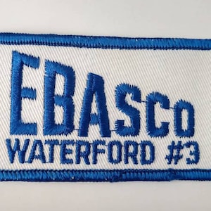 May include: Embroidered patch with a white background and blue border. The patch features the text "EBASCO WATERFORD #3" in blue, stitched in a bold, stylized font. The patch is rectangular.