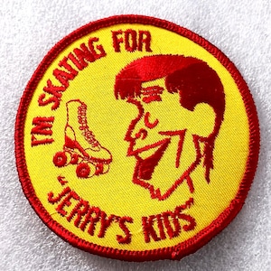 May include: A round, yellow patch with red trim and lettering. The text reads "I'M SKATING FOR JERRY'S KIDS" around the edge. A red roller skate and a cartoon profile are in the center.
