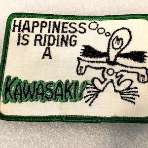 May include: Embroidered patch with a green border and the text "HAPPINESS IS RIDING A KAWASAKI!" in black and green. The patch features a cartoon figure with a thought bubble.