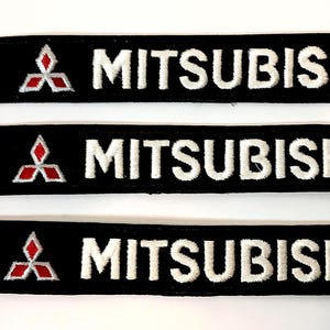 May include: Three black embroidered patches with the word "MITSUBISHI" in white block letters. Each patch features the Mitsubishi logo, a red three-diamond design, on the left side.