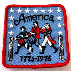 May include: Square patch with a red border and a light blue background. The patch features the word "America" above an illustration of three marching figures in colonial attire. The year range "1776-1976" is below the figures, with white stars above.