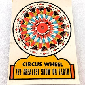 May include: Vintage circus-themed card featuring a colorful wheel design with red, orange, yellow, and blue segments. The card includes the text "CIRCUS WHEEL" and "THE GREATEST SHOW ON EARTH" in a yellow and orange banner.
