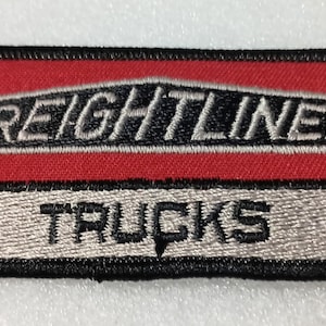 May include: Embroidered patch with the Freightliner Trucks logo. The patch has a red top section with the word "FREIGHTLINER" in white and black lettering. The bottom section is silver with the word "TRUCKS" in black.