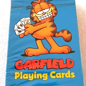 May include: A sealed deck of Garfield Playing Cards. The box is blue with a cartoon image of Garfield holding playing cards. The Garfield logo is in red and yellow. Copyright 1978 United Feature Syndicate, Inc.