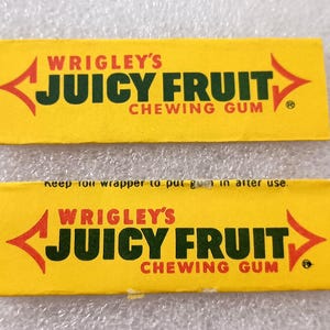 May include: Two yellow Wrigley's Juicy Fruit chewing gum wrappers. The wrappers have red and green text and arrows. The text reads "WRIGLEY'S JUICY FRUIT CHEWING GUM". One wrapper has the text "Keep foil wrapper to put gum in after use."