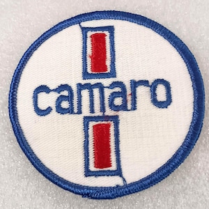 May include: A round, white patch with a blue border and the word "camaro" in blue script. Two red rectangles are positioned above and below the word, and two more red rectangles are positioned above and below the word.