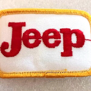 May include: A rectangular patch with the word "Jeep" embroidered in red on a white background. The patch has a yellow border with a stitched design.