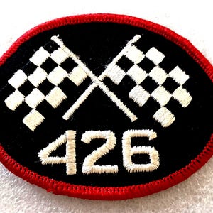 May include: An oval-shaped embroidered patch with a black background and a red stitched border. The design features two crossed white checkered racing flags above the white embroidered number 426, all rendered in a clean, high-contrast thread.