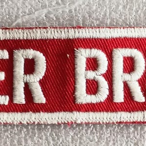 May include: Embroidered patch with the words "BADGER BREEDERS" in white, on a red background with a white border. The patch is rectangular and appears to be made of fabric. The text is in a bold, sans-serif font.