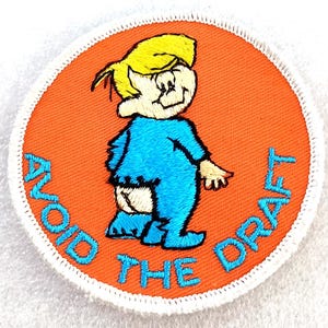 May include: Embroidered patch with a cartoon character in blue pajamas and yellow hair, with the text "AVOID THE DRAFT" in blue. The patch has an orange background and a white border.