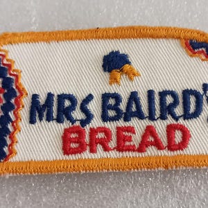 May include: Embroidered patch with the text "MRS BAIRD'S BREAD" in navy blue and red, with a small blue and yellow design above the text. The patch has a white background with orange and blue decorative edges.