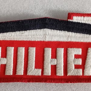 May include: Embroidered patch with the word "PHILHEAT" in white block letters on a red background. The patch features a black and white roof design and a small chimney. The patch is rectangular in shape.
