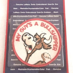 May include: Embroidered patch with the text "MY GUYS A BULLSHIPPER" in a circular design. The patch features a cartoon bull illustration. The patch is on a LeMans branded backing card.