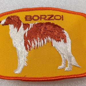 May include: Embroidered patch featuring a Borzoi dog in profile. The dog is depicted in white and brown thread against a yellow background. The word "BORZOI" is embroidered above the dog. The patch has an orange border.