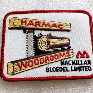 May include: Embroidered patch with a red border and a white background. The patch features the words "HARMAC" and "WOODROOMS" in red, with a saw and log design. The text "MACMILLAN BLOEDEL LIMITED" is also present.