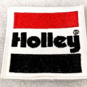 May include: Square white patch with the word "Holley" in black, bold letters. The top section is red, and the bottom section is black. The patch has a white border and a small registered trademark symbol.