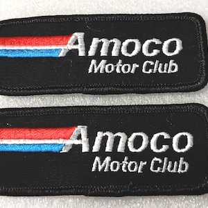 May include: Two black embroidered patches with the text "Amoco Motor Club". Each patch has a horizontal stripe of red and blue above the text. The patches are rectangular with rounded corners.