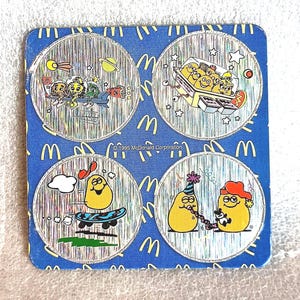 May include: A vintage McDonald's promotional coaster featuring four circular images of anthropomorphic McNuggets. The background is blue with repeating yellow "M" logos. The coaster is from 1995.