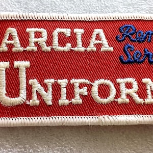 May include: Embroidered patch with the text "GARCIA UNIFORMS Rental Service." The patch has a red background with white and blue embroidered lettering. The patch is rectangular with a white border.