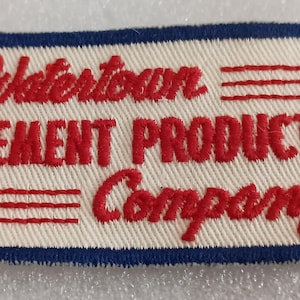 May include: Embroidered patch with the text "Watertown CEMENT PRODUCTS Company" in red on an off-white background. The patch has a blue border and red horizontal lines.