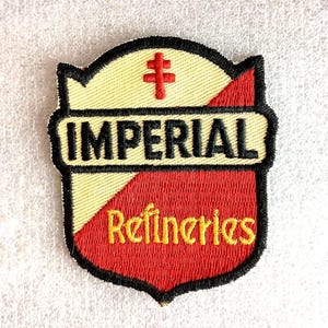 May include: Embroidered patch with a shield design. The patch features the word "IMPERIAL" in black letters on a yellow background. Below, the word "Refineries" is in yellow script on a red background. A red cross is at the top.