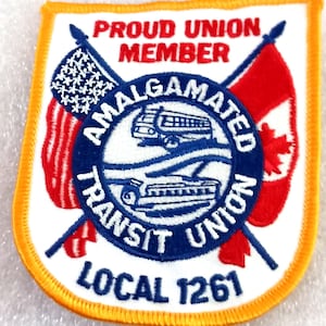 May include: Embroidered patch with a white background and an orange border. The patch features the text "PROUD UNION MEMBER" and "AMALGAMATED TRANSIT UNION LOCAL 1261". It also includes images of a bus, a train, and the flags of the United States and Canada.