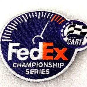 May include: Embroidered patch featuring the FedEx logo with the text "CHAMPIONSHIP SERIES." The patch has a speedometer design with a checkered flag and the word "CART." The colors are navy blue, white, and orange.