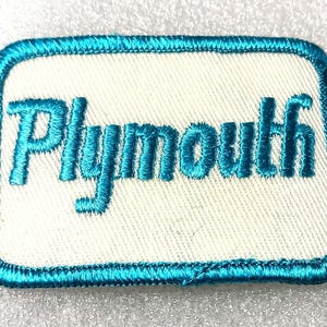 May include: A rectangular patch with a white background and a teal border. The word "Plymouth" is embroidered in teal across the center. The patch has rounded corners and a textured appearance.