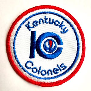 May include: Embroidered patch featuring the words "Kentucky Colonels" in blue, arched around a white circle. The center has a blue "KC" logo with a red and white design. The patch has a red border.