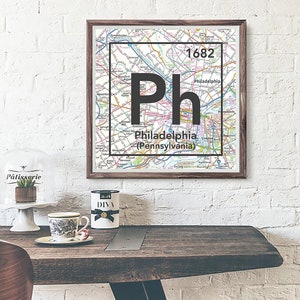 May include: A framed map of Philadelphia, Pennsylvania, designed to look like a periodic table element. The element symbol is "Ph" and the atomic number is "1682".