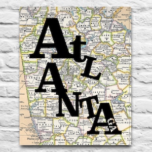 May include: A vintage map of Georgia with the word "Atlanta" in large black letters superimposed on top of the map. The map shows the state of Georgia with county names and major cities.