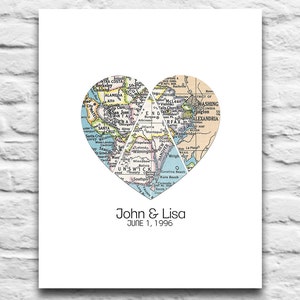 Puede incluir: Impresión enmarcada con un diseño de mapa en forma de corazón, dividido en tres partes. El mapa muestra varias ubicaciones, con los nombres "John & Lisa" y "JUNE 1, 1996" impresos debajo. La impresión está sobre un fondo blanco.