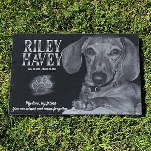 Puede incluir: Un monumento conmemorativo para mascotas de granito negro con el nombre "RILEY HAVEY" y las fechas 23 de junio de 2008 - 20 de marzo de 2017. Presenta una imagen grabada detallada de un perro y una huella de pata. La inscripci&oacute;n dice "Mi amor, mi amigo, Te echamos de menos y nunca te olvidaremos."