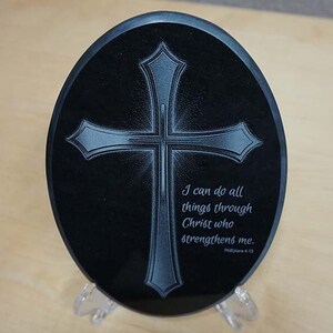 May include: A black oval-shaped stone with a silver cross engraved on it. The stone has the text "I can do all things through Christ who strengthens me. Philippians 4:13" engraved on it.