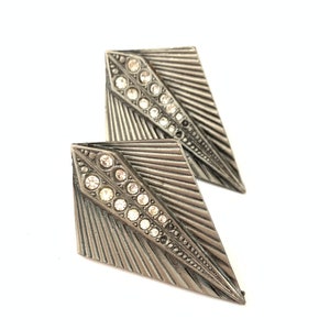May include: A pair of silver tone earrings with a geometric design and clear rhinestones.