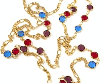 May include: A gold-toned necklace with a chain design, featuring alternating red, blue, and purple gemstone accents. The gemstones are round and set in gold bezels. The necklace is displayed against a white background.