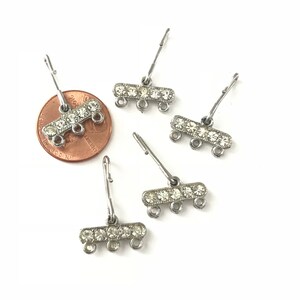 May include: Five silver-toned metal jewelry connectors with three loops and a row of clear rhinestones. The connectors are about the size of a US penny.