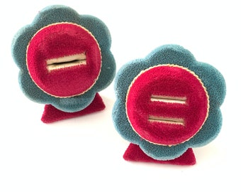May include: Two blue velvet ring holders shaped like flowers with red velvet centers. Each holder has a slot for a ring.